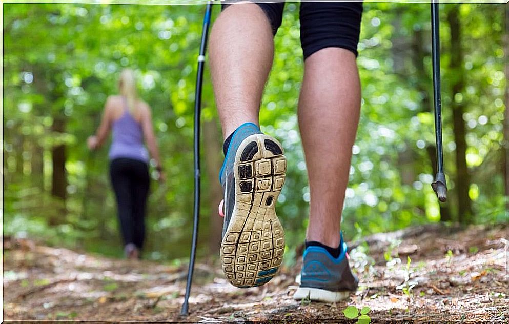 Feet with sports shoes and poles together with a woman in the background practicing Nordic walking.